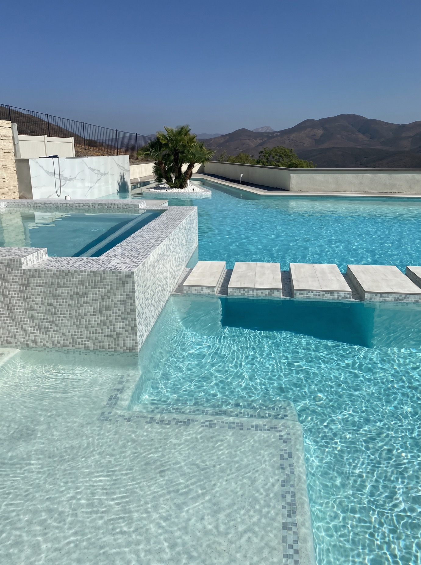 Mosaic-tile infinity pool and spa with floating concrete steps at sunset